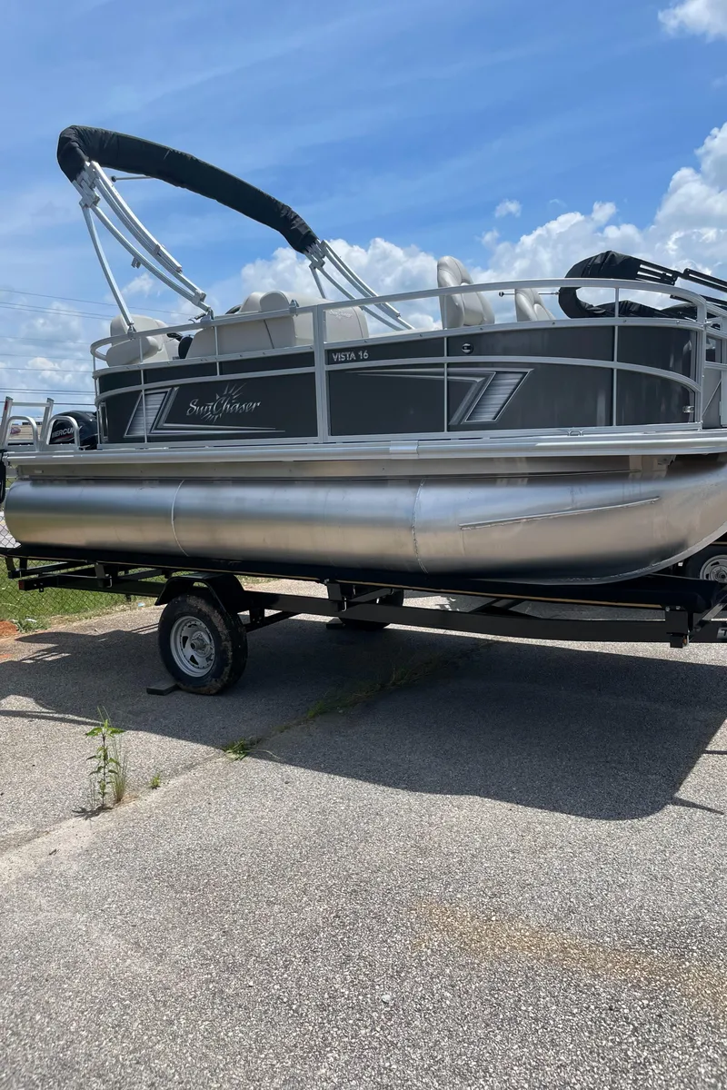 Slide: The Image of 2023 SunChaser Vista 16 Fish pontoon boat on a trailer under a blue sky. - 1