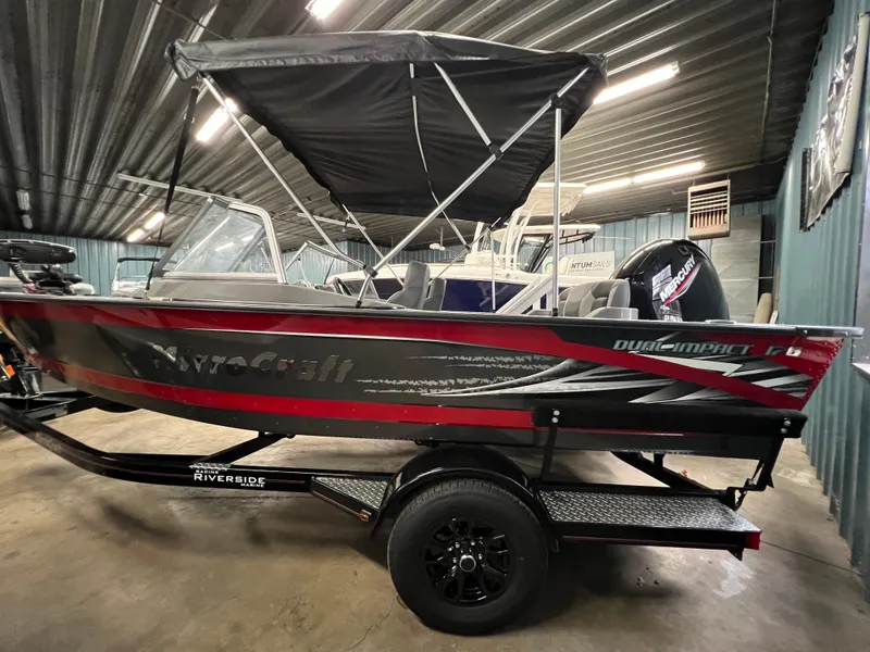 Slide: The Image of 2023 MirroCraft 176 Dual Impact boat in a garage, featuring a sleek design and canopy. - 2