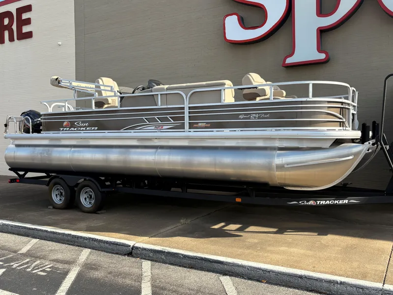 The Image of 2023 Sun Tracker Sportfish 24 XP3 pontoon boat on trailer, parked outside a store. - 0