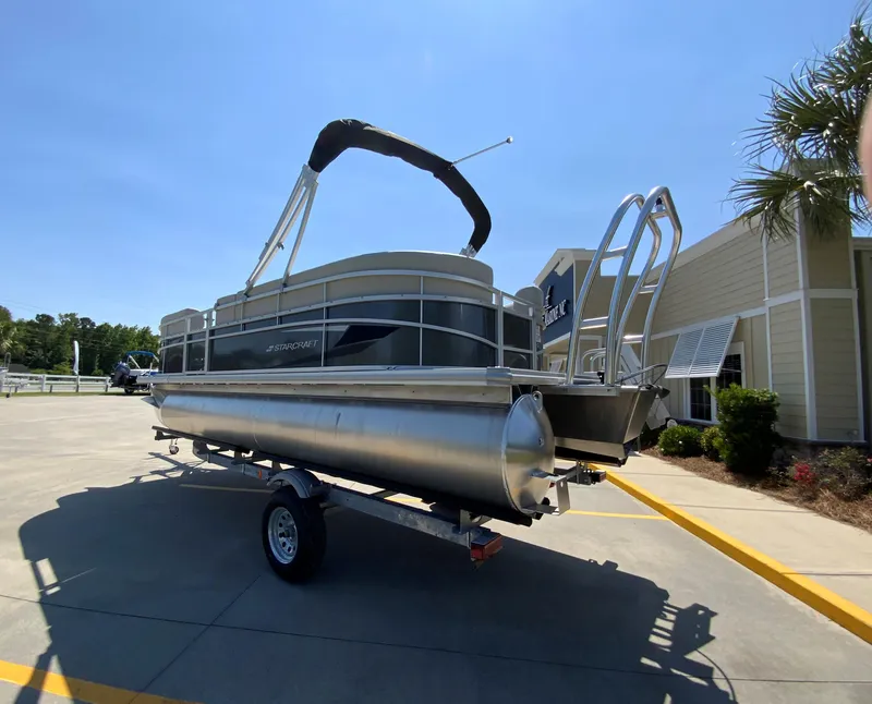 Slide: The Image of 2024 Starcraft LX20 R pontoon boat on a trailer in a sunny outdoor setting. - 4