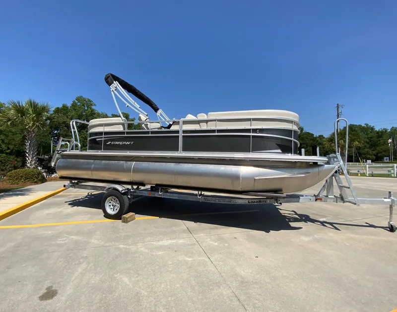 Slide: The Image of 2024 Starcraft LX20 R pontoon boat on a trailer in a parking lot. - 1