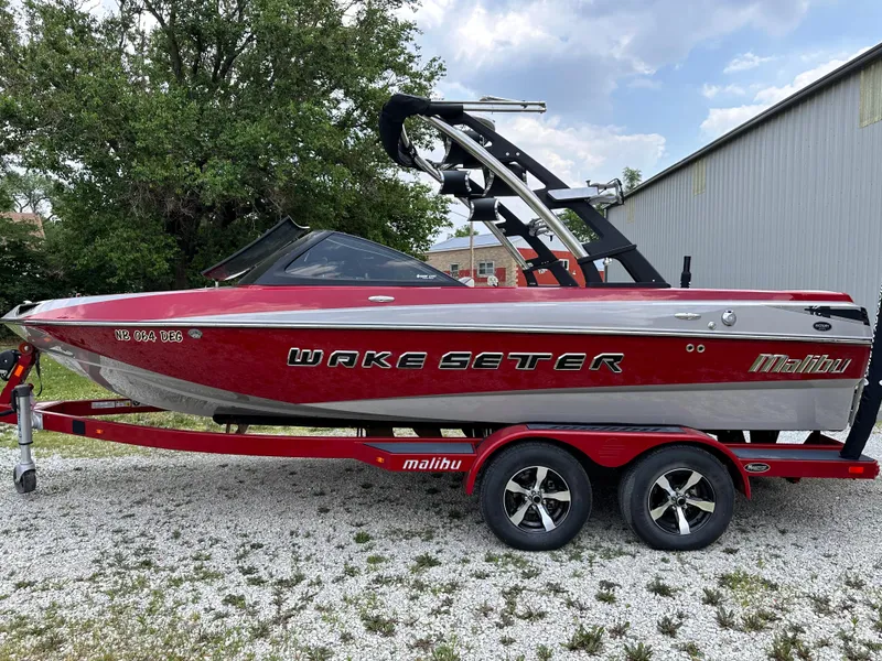 The Image of 2014 Malibu VTX Wakesetter boat on a red trailer, parked outdoors. - 1