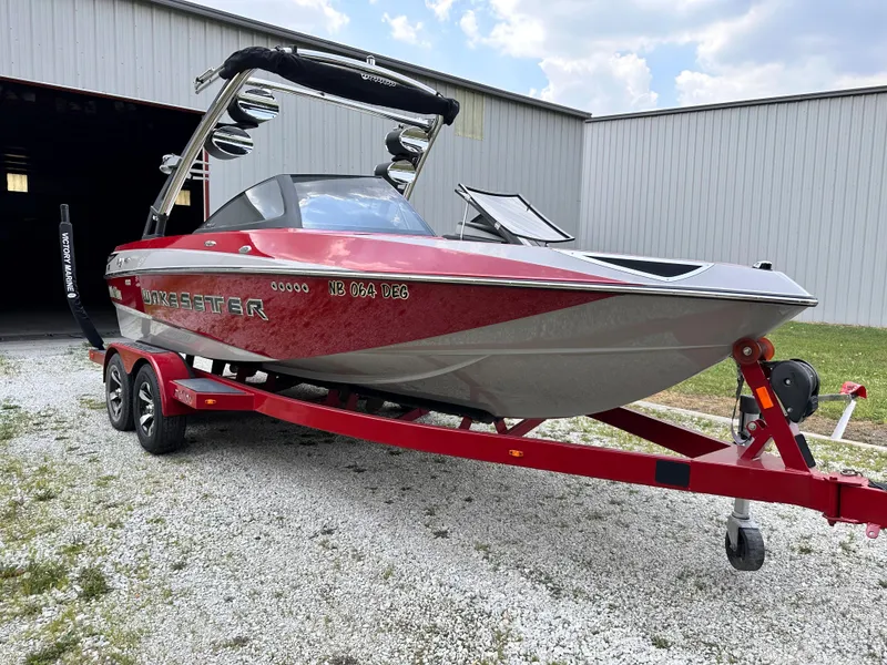 Slide: The Image of 2014 Malibu VTX Wakesetter boat on a red trailer outside a storage building. - 5