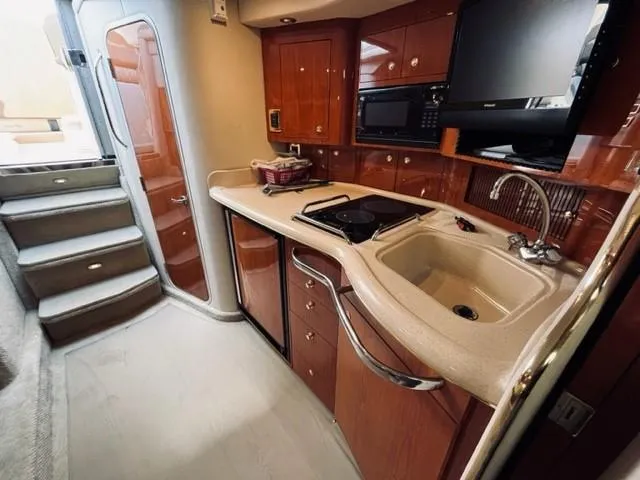 Slide: The Image of 2001 Sea Ray 340 AJ yacht interior kitchen with sink, stove, microwave, and wooden cabinetry. - 23