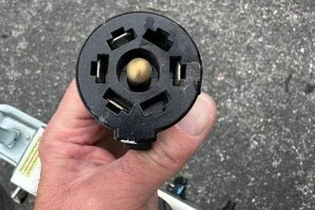 Slide: The Image of Close-up of a hand holding a boat plug connector for a 2023 Mako SKIFF 19 CC. - 2