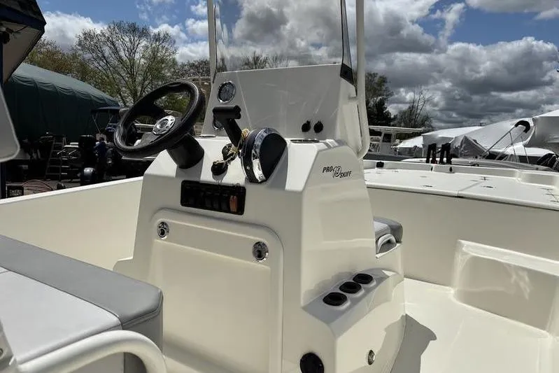 Slide: The Image of 2023 Mako SKIFF 19 CC boat console with steering wheel and controls under cloudy sky. - 21