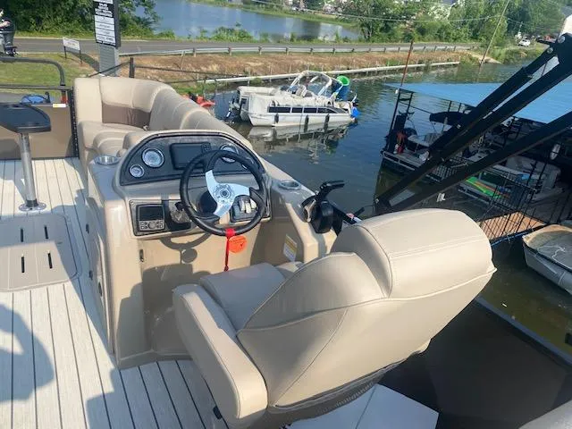 Slide: The Image of 2023 SunCatcher Fusion 324SS boat interior with steering wheel and seating, docked by a lake. - 17