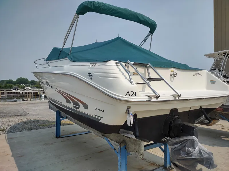The Image of 1997 Sea Ray 240 SIGNATURE boat with green canopy on a stand, dockside view. - 0