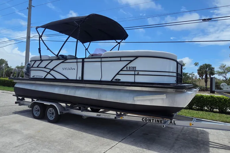 Slide: The Image of 2022 Sylvan Mirage X X3 pontoon boat on trailer, parked outdoors under blue sky. - 8