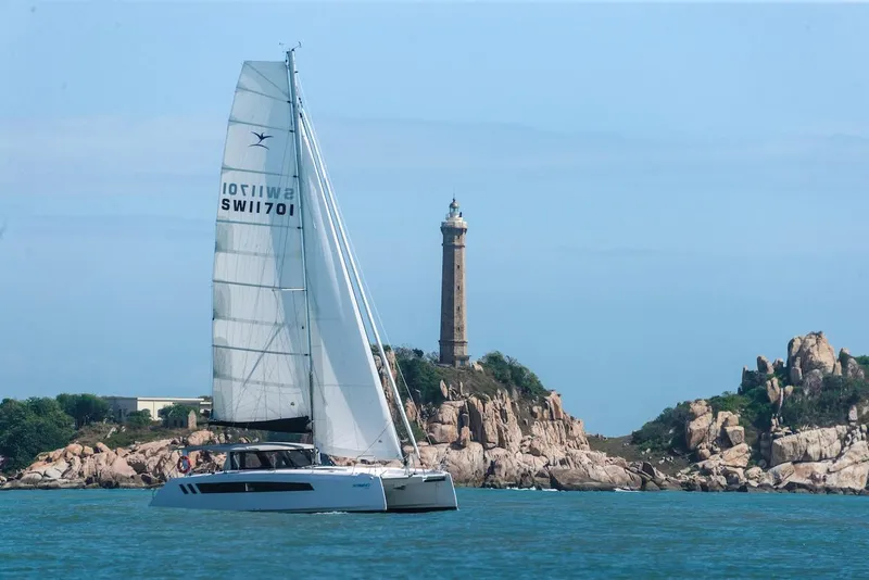 Slide: The Image of 2025 Seawind 1170 catamaran sailing near rocky coastline with lighthouse in background. - 12