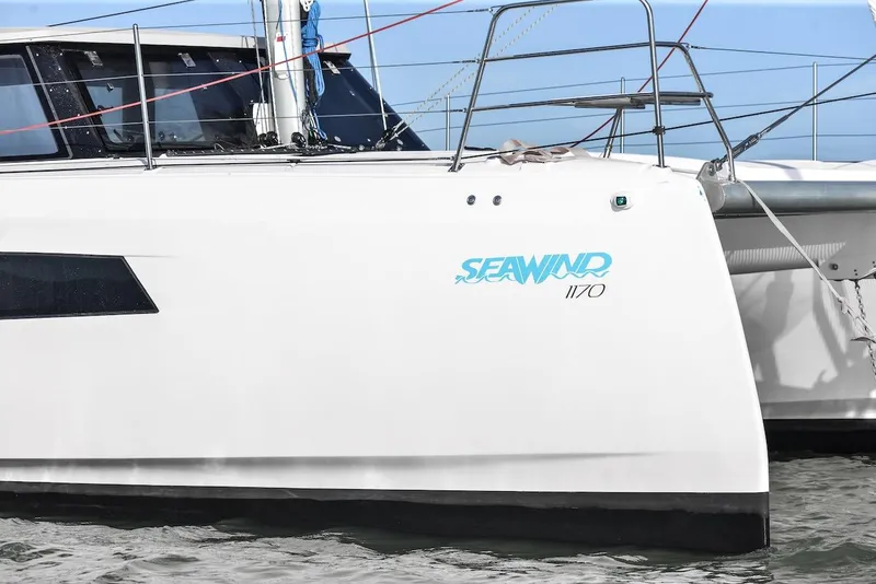 Slide: The Image of 2025 Seawind 1170 catamaran side view with logo, docked on calm water. - 2