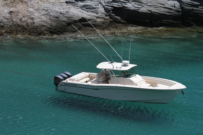 Slide: The Image of 2024 Grady-White Canyon 386 boat anchored in clear turquoise water near rocky shore. - 0