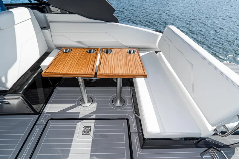 Slide: The Image of 2025 Cruisers Yachts 34 GLS interior with sleek seating and wooden tables on a sunny day. - 19