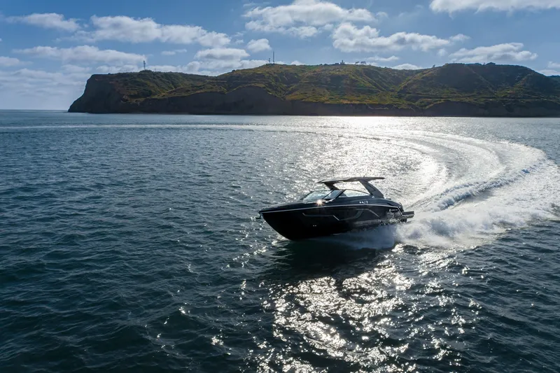 Slide: The Image of 2025 Cruisers Yachts 34 GLS speeding on open water with scenic coastline backdrop. - 2