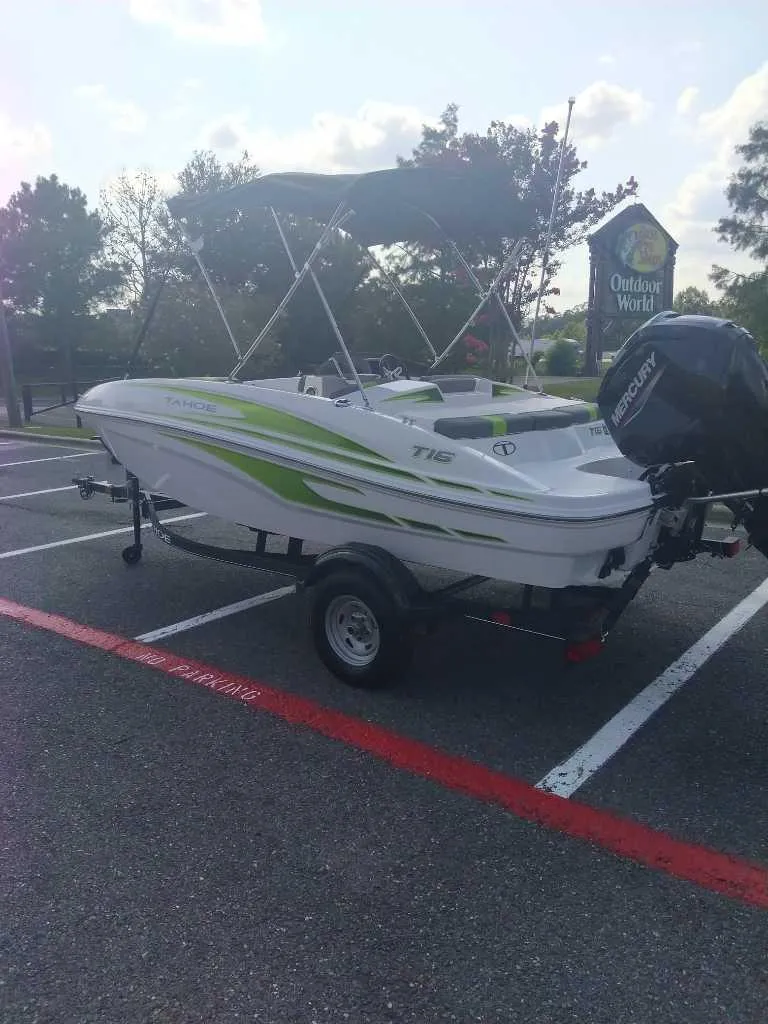 The Image of 2023 Tahoe T16 boat with green accents on a trailer in a parking lot. - 0