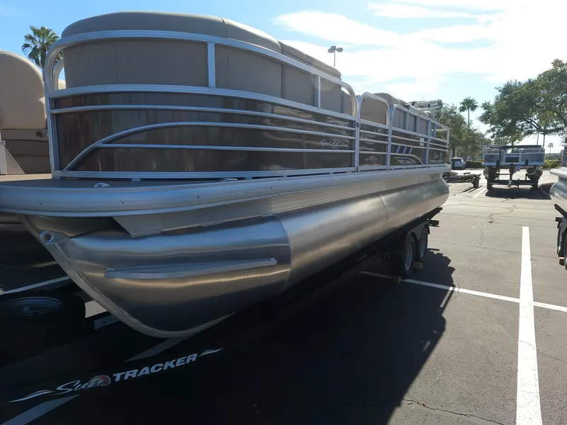 The Image of 2023 Sun Tracker SportFish 22 XP3 pontoon boat on a trailer in a parking lot. - 0