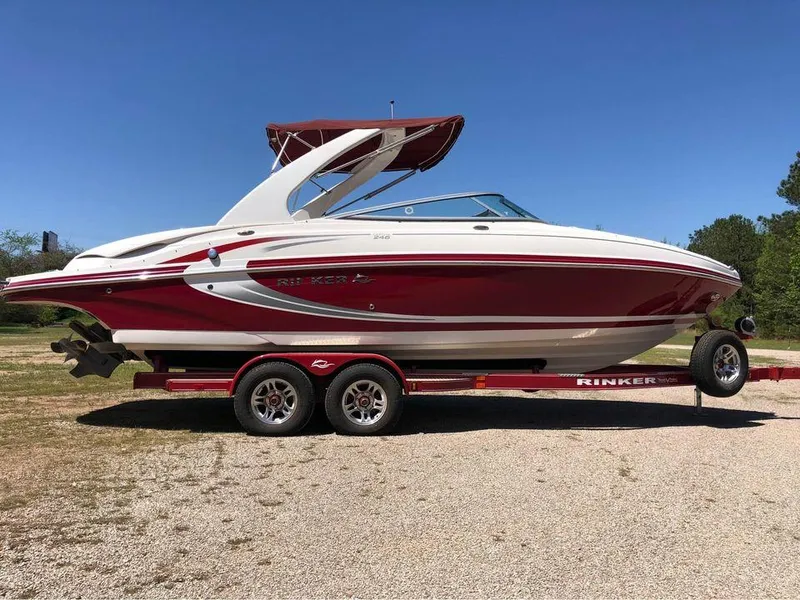 The Image of 2013 Rinker 246 Captiva Bowrider boat on trailer, red and white design, sunny day. - 0