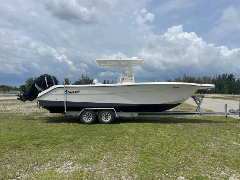 Slide: The Image of 2006 Angler 2900CC boat on a trailer, parked on grassy area under cloudy sky. - 0