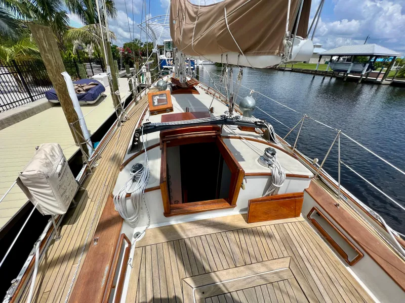 Slide: The Image of 1986 Cherubini 44 sailboat with wooden deck and open hatch, docked by a canal. - 21