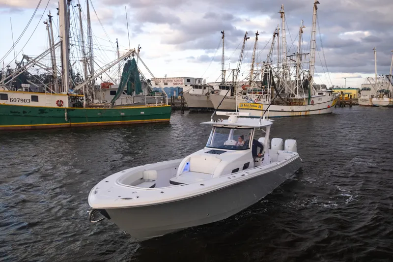 Slide: The Image of 2024 Edgewater 370CC boat cruising in a harbor with fishing vessels. - 0