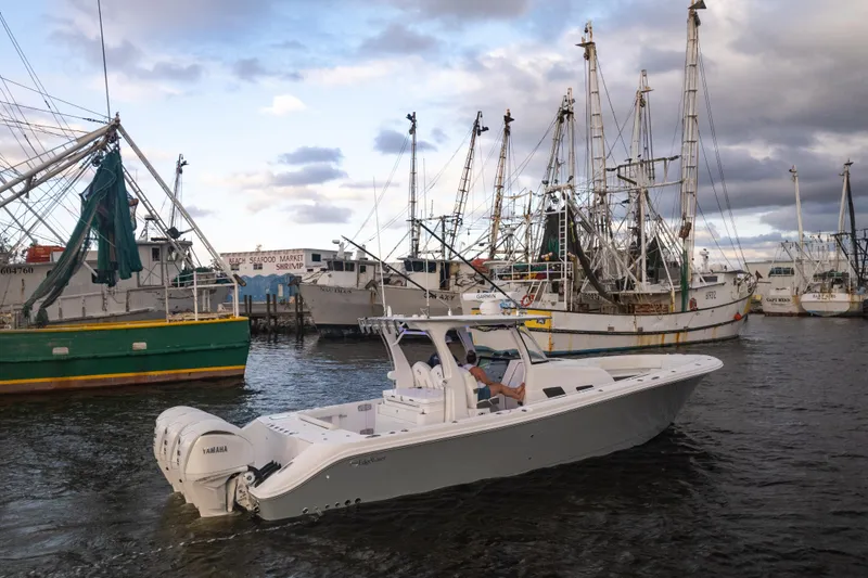 Slide: The Image of 2024 Edgewater 370CC boat cruising near fishing vessels in a harbor. - 1