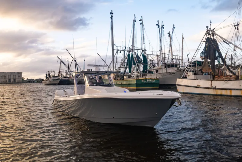 Slide: The Image of 2024 Edgewater 370CC boat cruising in a marina with fishing boats. - 34