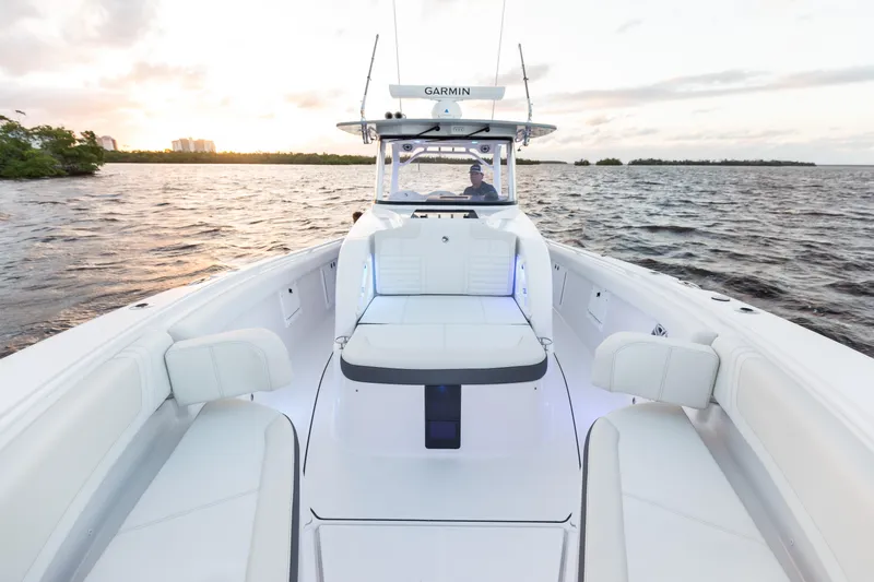Slide: The Image of 2024 Edgewater 370CC boat interior with white seating, on a calm water body at sunset. - 7