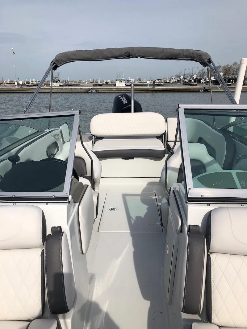 Slide: The Image of 2023 Crownline E 215 XS boat with white and gray interior, docked by the water. - 2