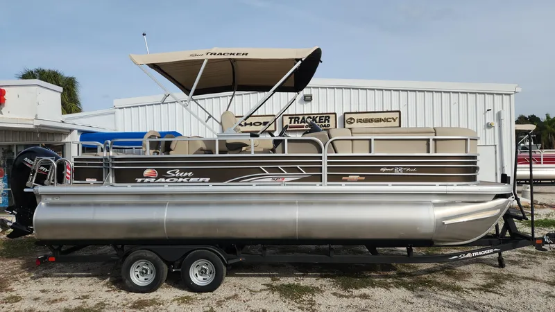 The Image of 2023 Sun Tracker SportFish 22 XP3 pontoon boat on trailer, parked outside dealership. - 0