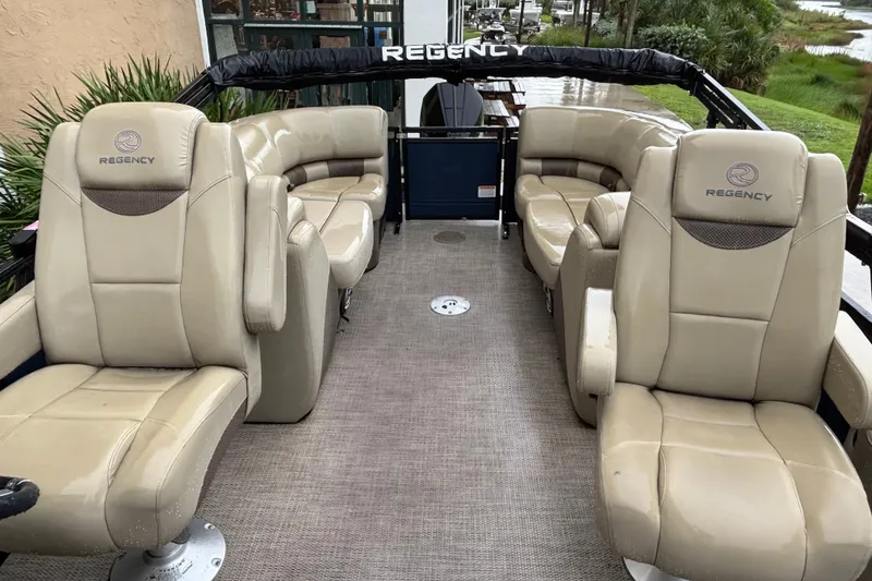 Slide: The Image of 2023 Regency 230 LE3 pontoon boat interior with beige seating and spacious layout. - 2