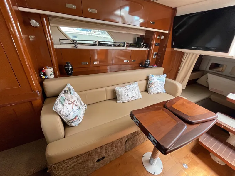 Slide: The Image of Interior of 2012 Sea Ray 350 Sundancer with beige sofa, wooden table, and TV. - 19
