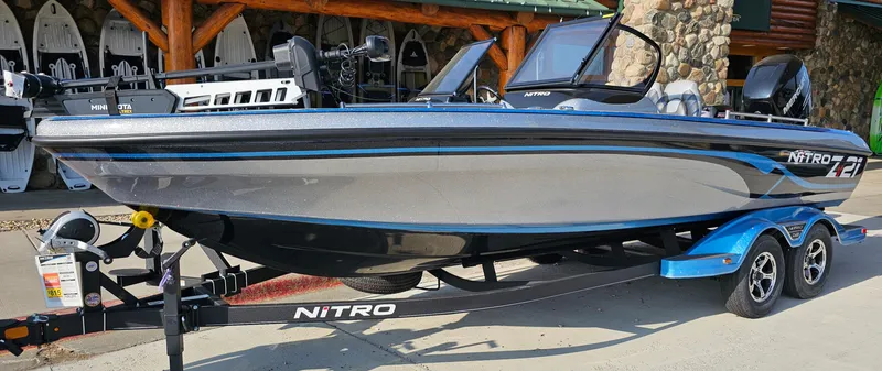 Slide: The Image of 2023 Nitro ZV21 boat on a trailer, parked outside a rustic building. - 0