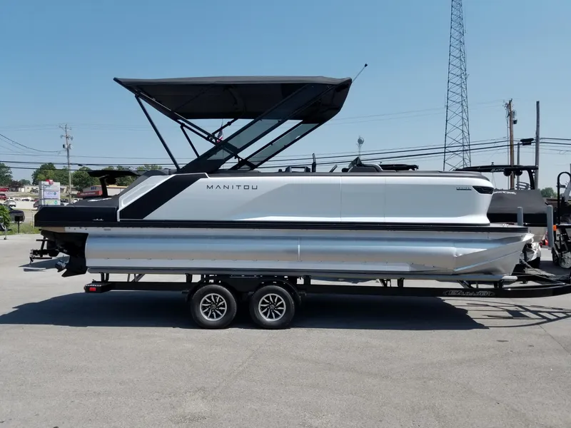 The Image of 2025 Manitou Cruise pontoon boat on a trailer in a parking lot. - 0