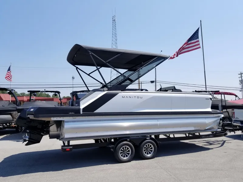Slide: The Image of 2025 Manitou Cruise pontoon boat on a trailer with American flags in the background. - 17