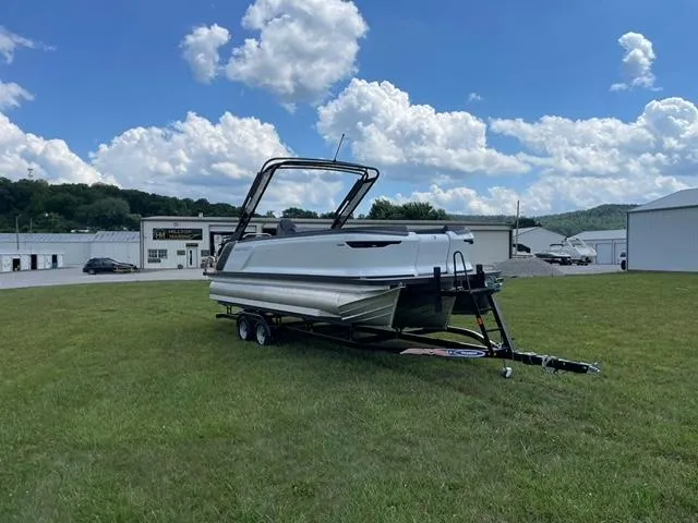 Slide: The Image of 2023 Manitou 24 Explore SB with 250 hp Mercury on trailer, grassy field background. - 1
