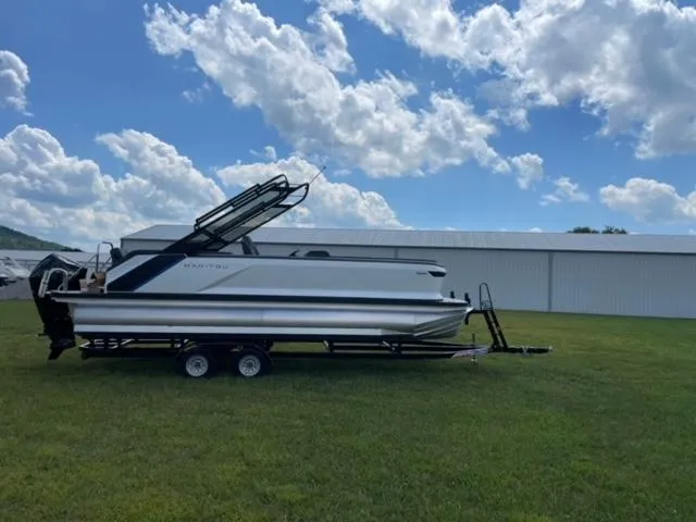 Slide: The Image of 2023 Manitou 24 Explore SB with 250 hp Mercury on trailer, under blue sky. - 2