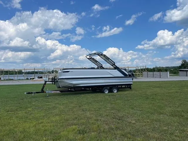 Slide: The Image of 2023 Manitou 24 Explore SB with 250 hp Mercury on trailer, grassy field background. - 3