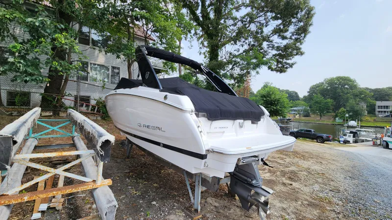 Slide: The Image of 2017 Regal 22 FasDeck boat on land, covered, near trees and water. - 25