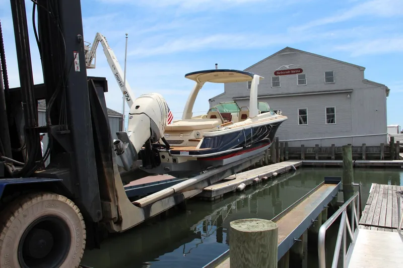 Slide: The Image of 2022 Chris-Craft Launch 25 GT boat being lifted at a marina dock. - 2