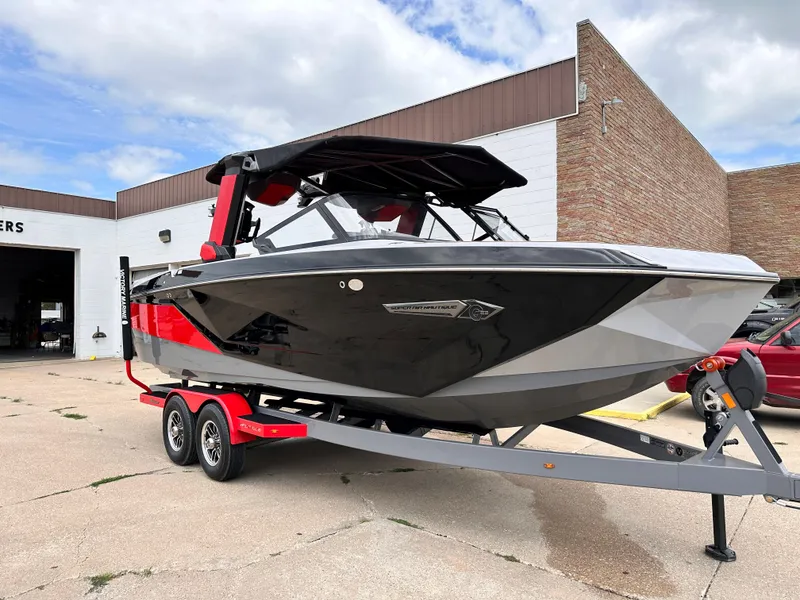 Slide: The Image of 2023 Nautique G23 boat on a trailer outside a building under a partly cloudy sky. - 2