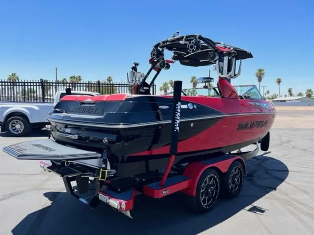 Slide: The Image of 2014 Supra SC350-550 boat, red and black, on a trailer in a sunny outdoor setting. - 6