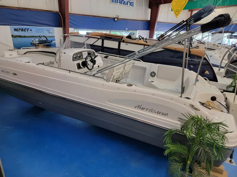 The Image of 2024 Hurricane SunDeck Sport CC 231 OB boat displayed indoors with promotional banners. - 0