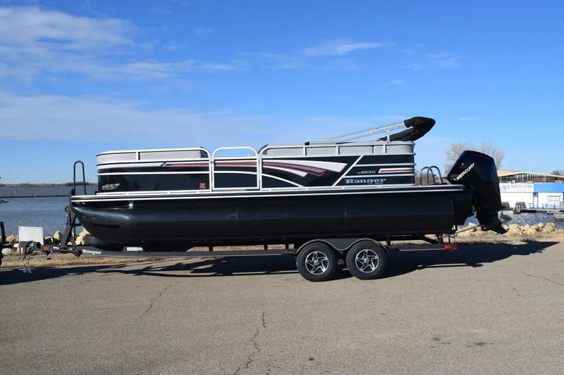 Slide: The Image of 2023 Ranger 223C pontoon boat on a trailer by the water. - 0