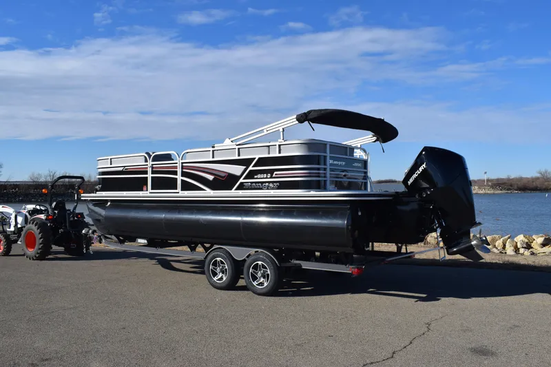 Slide: The Image of 2023 Ranger 223C pontoon boat on a trailer by the water. - 2