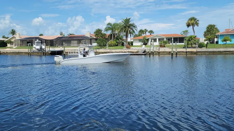 Slide: The Image of 2005 Yellowfin 31 boat cruising on a sunny waterfront with palm trees and houses. - 34