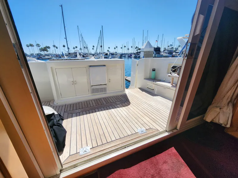 Slide: The Image of 1999 McKinna 57 Pilothouse yacht deck with marina view, featuring wooden flooring and storage cabinets. - 2