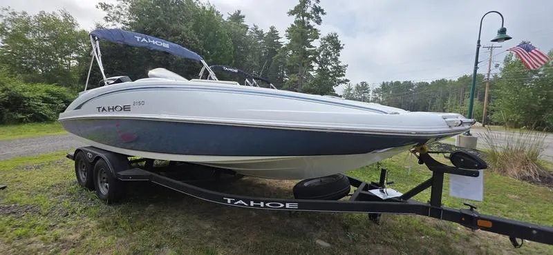 Slide: The Image of 2024 Tahoe 2150 boat on trailer, parked outdoors with trees and American flag in background. - 4