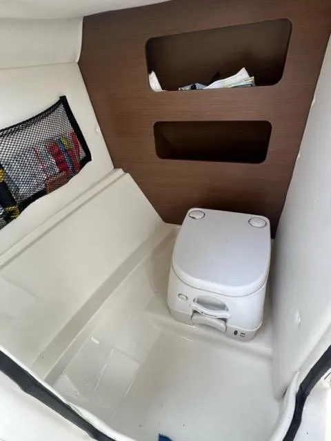 Slide: The Image of 2013 Sea Ray 240 Sundeck interior with portable toilet and storage shelves. - 21