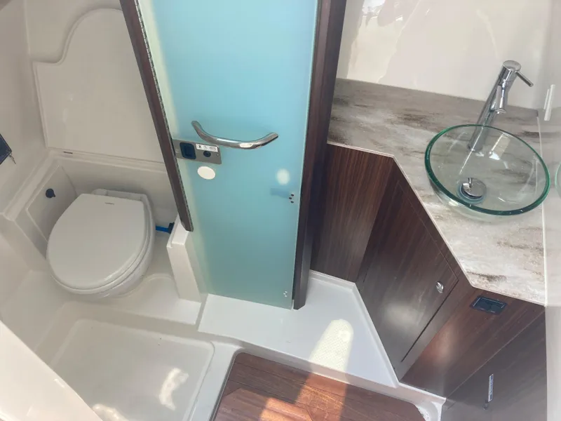 Slide: The Image of 2023 Pursuit DC 365 boat bathroom with toilet, sink, and frosted glass door. - 10
