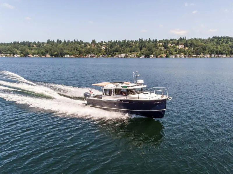 The Image of 2024 Ranger Tugs R-27 cruising on a lake with a scenic shoreline in the background. - 1